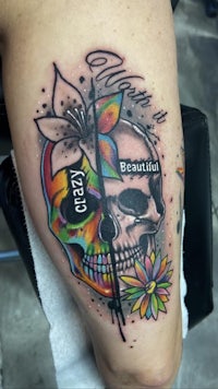 a tattoo with a skull and flowers on the thigh