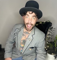 a man with tattoos and a top hat sitting on a chair